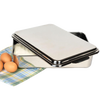 Open rectangular stainless steel cake pan with lid resting on a plaid cloth next to three brown eggs, ideal for baking and holiday hosting in the kitchen.