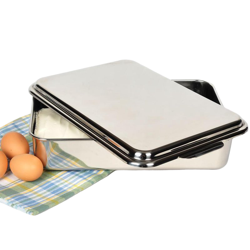 Open rectangular stainless steel cake pan with lid resting on a plaid cloth next to three brown eggs, ideal for baking and holiday hosting in the kitchen.
