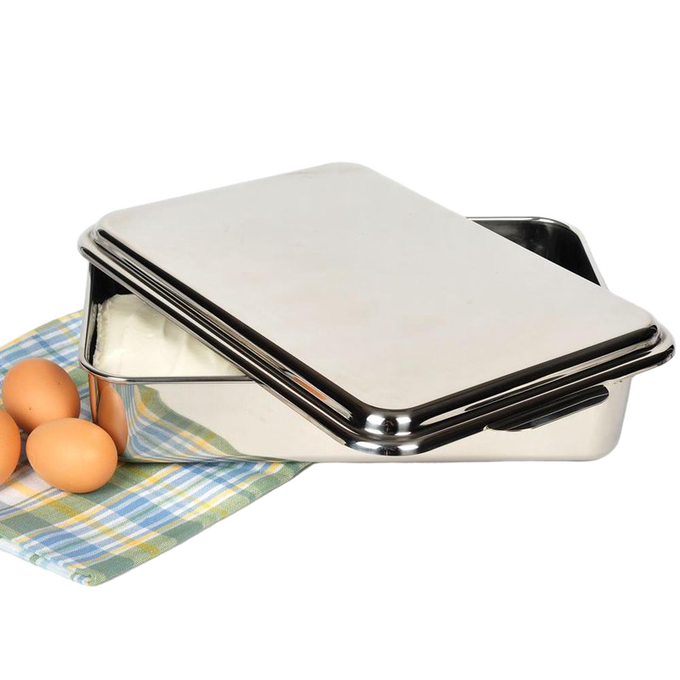 Open rectangular stainless steel cake pan with lid resting on a plaid cloth next to three brown eggs, ideal for baking and holiday hosting in the kitchen.