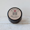 Small amber glass jar of handcrafted all-natural face cream with a simple kraft paper label, featured in Health & Wellness and USA Made collections.