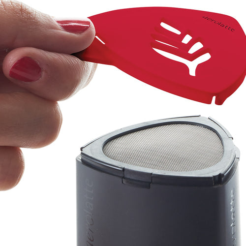 Hand holding a red stencil featuring a leaf pattern above a black powder shaker with a mesh top, designed for creating decorative cappuccino art, featured in Kitchen & Food and Brewing Coffee and Tea collections.