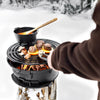 Cast iron fire grill with adjustable grate cooking steaks, mushrooms, and a pot over an open flame in winter setting, ideal for camping, grilling, and farm tool collections.