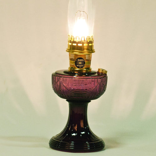 Glowing handcrafted oil lamp with a purple glass Lincoln drape base, clear chimney, and polished brass burner, ideal for Farm, Garden & Tool, Lamps & Lighting, Oil Lamps, and Homesteading collections.