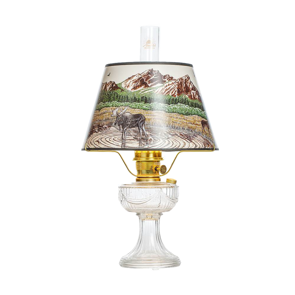 Clear oil lamp with brass burner and a Rocky Mountain scenic parchment shade depicting a moose by a lake with mountains in the background, featured in Lamps & Lighting, Oil Lamps, Table Lamps, Best Sellers, and Promo Eligible collections.