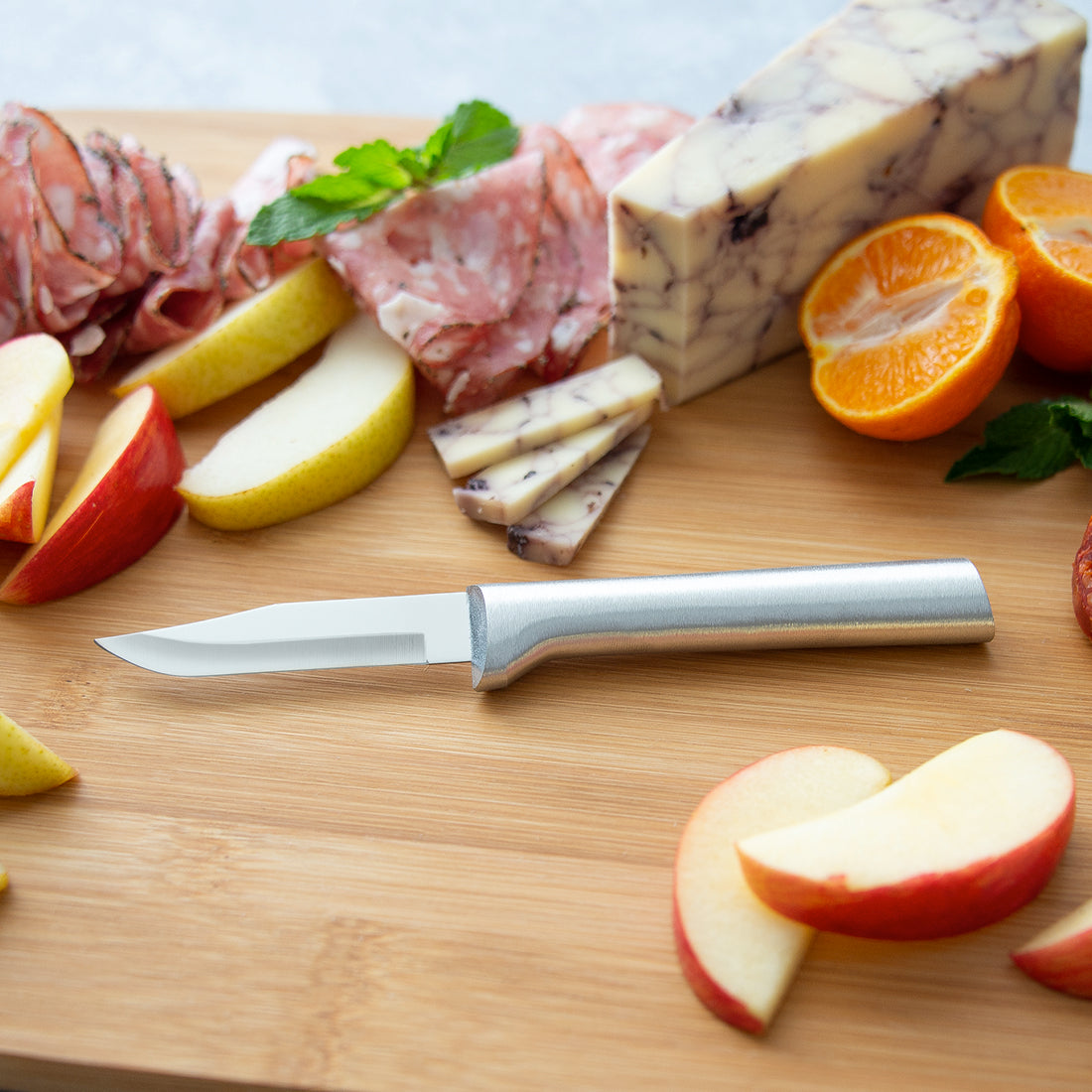 Paring knife with a sharp carbon stainless steel blade and satin-finished cast aluminum handle, set on a wooden board with sliced apples, cheese, cured meats, and fresh fruit, ideal for food prep in USA made and best sellers collections.