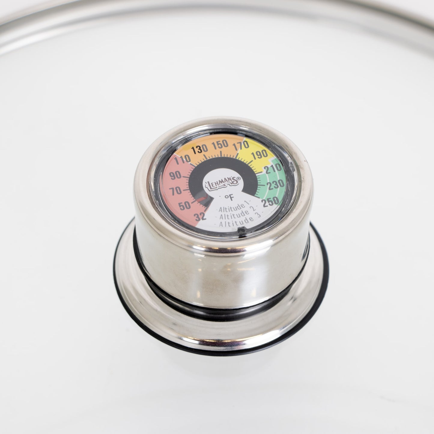 Close-up of a stainless steel built-in temperature gauge on a glass lid with color-coded heat zones, designed for precise monitoring in canning, food preservation, and kitchen use.