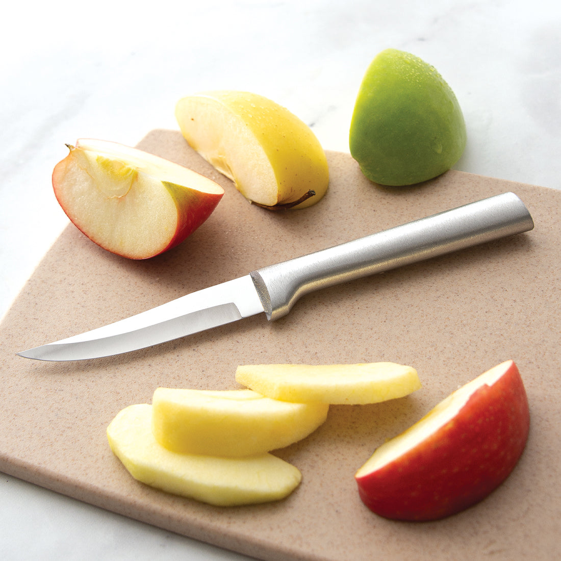 Rada paring knife with a carbon stainless steel blade and durable cast aluminum handle featuring a non-slip satin finish, shown slicing fresh apple wedges on a cutting board, ideal for Kitchen & Food and USA Made collections.