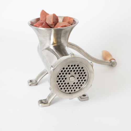 Handcrafted stainless steel kitchen-mounted meat grinder with wooden handle and chunks of fresh meat in hopper, featured in Kitchen & Food, Specialty Equipment, and Butchering Supplies collections.