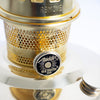 Close-up of a polished brass oil lamp burner with perforated ventilation, featuring an adjustable wick knob labeled for maximum brightness, part of a handcrafted lighting collection ideal for farm, garden, and emergency use.