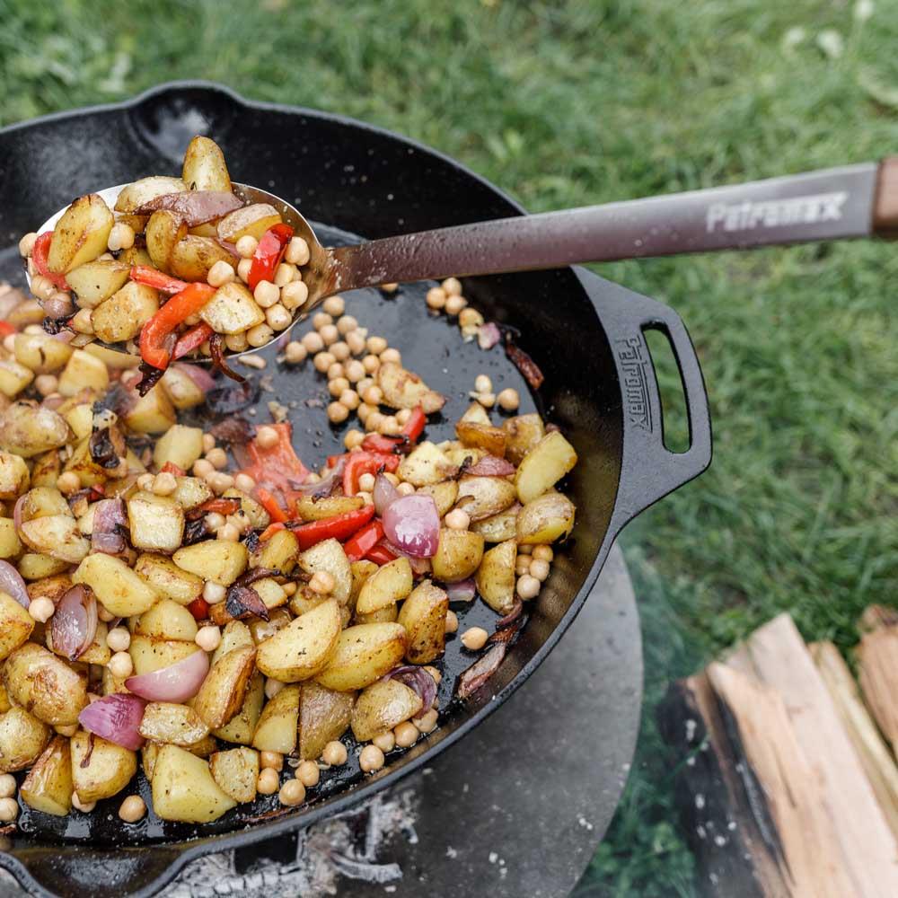 Cast iron skillet with two side handles cooking seasoned potatoes, red peppers, onions, and chickpeas over an outdoor fire, ideal for farm, kitchen, camping, cookware, and cast iron collections.