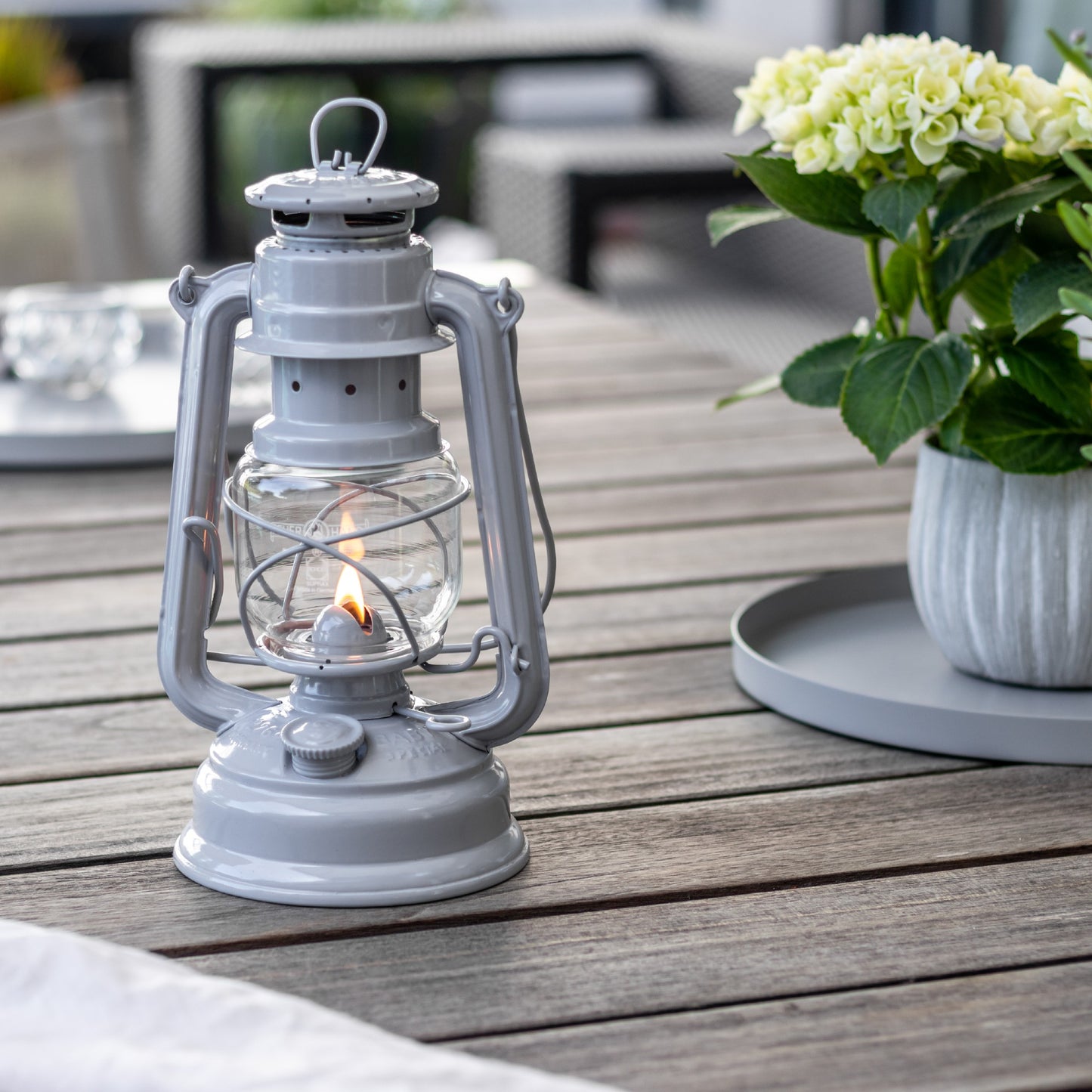 Handcrafted light gray galvanized oil lantern with thermal heat-resistant globe, softly glowing on an outdoor wooden table, ideal for Lamps & Lighting, Camping, and Emergency Supplies collections.