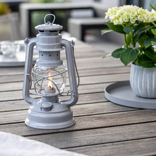 Handcrafted light gray galvanized oil lantern with thermal heat-resistant globe, softly glowing on an outdoor wooden table, ideal for Lamps & Lighting, Camping, and Emergency Supplies collections.
