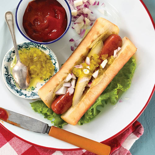 Freshly prepared New England-style hot dog on a soft bun with relish, chopped onions, and pickle spear, served on a lettuce-lined plate with ketchup and chopped onions, Kitchen & Food and Bread Making Supplies collections.
