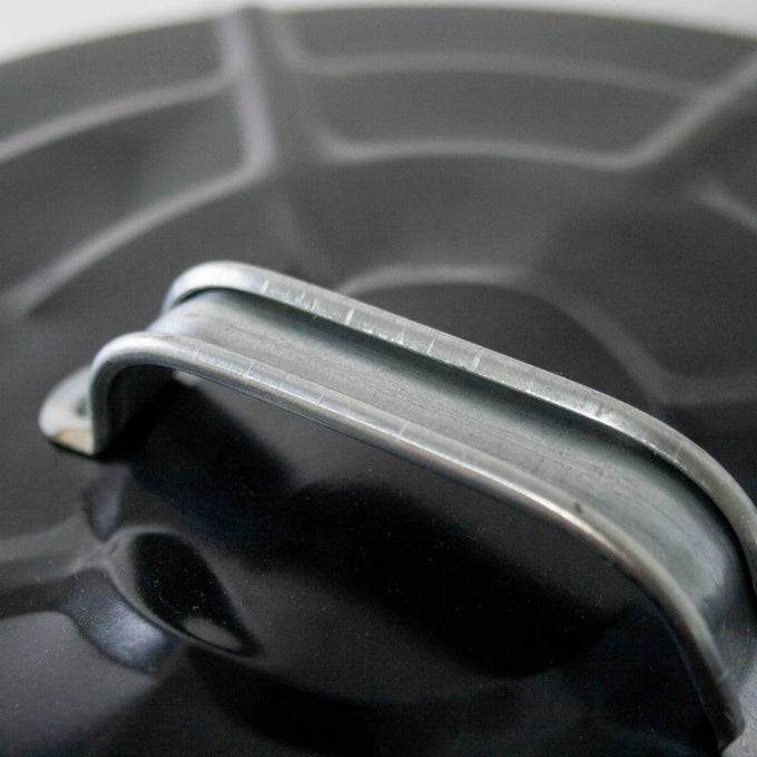 Close-up of a strong metal bail handle attached to a black painted steel lid, designed for secure lifting on a handcrafted ash pail used with stoves and hearth accessories in best sellers and promo collections.