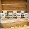 Seven uniquely scented handmade bar soaps in eco-friendly packaging arranged on a rustic wooden shelf, highlighting natural ingredients and handcrafted USA made wellness products.
