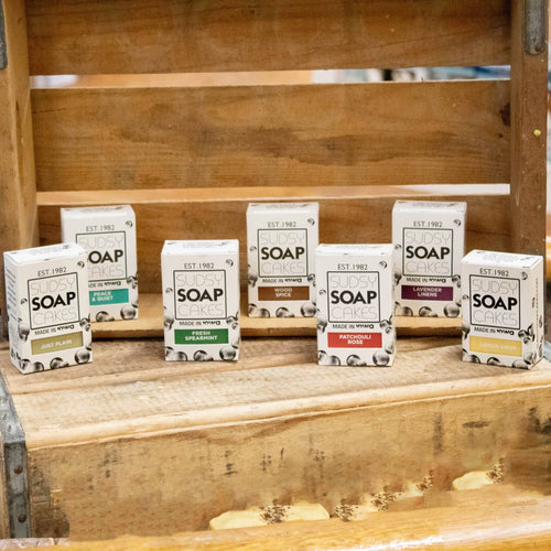 Seven uniquely scented handmade bar soaps in eco-friendly packaging arranged on a rustic wooden shelf, highlighting natural ingredients and handcrafted USA made wellness products.