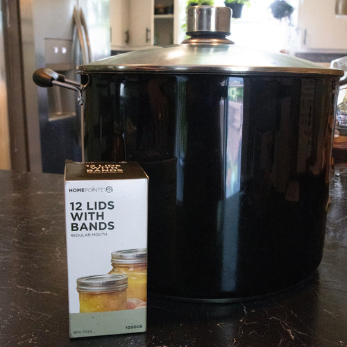 Box of 12 regular-mouth jar lids with bands featuring BPA-free sealing compound displayed on a kitchen counter next to a large black cooking pot, ideal for kitchen food preservation and canning collections.