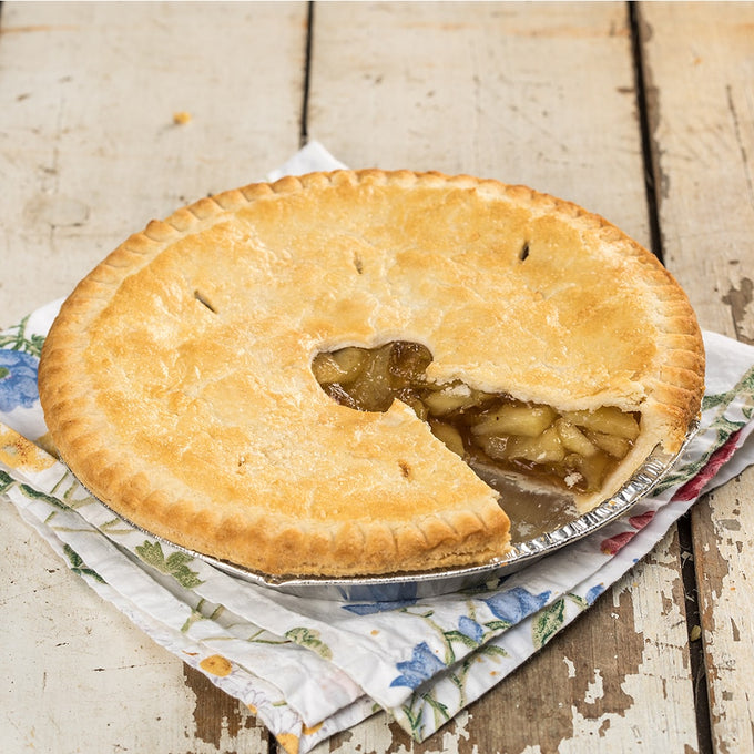 Golden brown homemade apple pie with a flaky crust and sweet, spiced apple filling, resting on a floral cloth on rustic wooden surface, perfect for farm and kitchen collections.