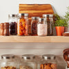 Three wide-mouth jars with sleek stainless steel lids arranged on a kitchen shelf, surrounded by dried fruits, spices, wooden salt and pepper shakers, a wooden cutting board, and a small potted plant, showcasing elegant storage in Kitchen & Food and Storage and Serving collections.