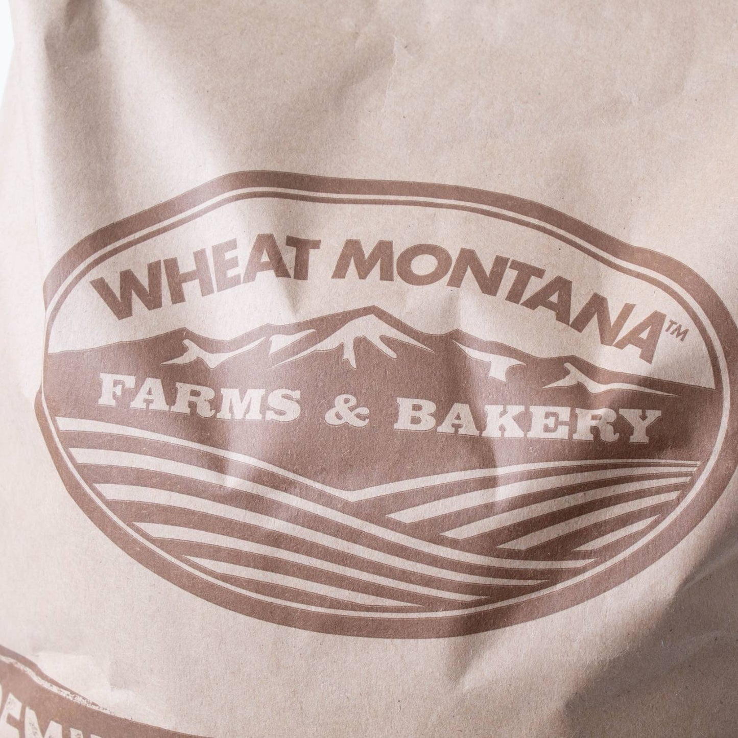 Close-up of a brown paper bag labeled with a rustic Montana Farms & Bakery logo featuring stylized mountains and farmland, suited for Farm, Garden & Tool, Kitchen & Food, and Pantry collections.