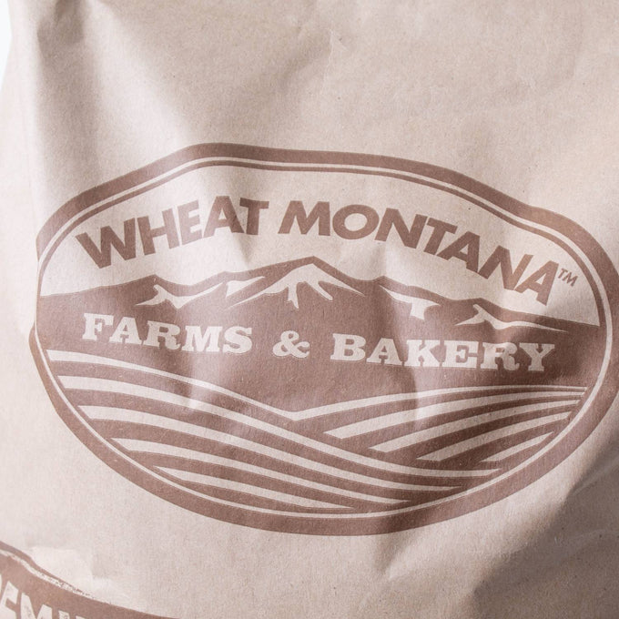 Close-up of a brown paper bag labeled with a rustic Montana Farms & Bakery logo featuring stylized mountains and farmland, suited for Farm, Garden & Tool, Kitchen & Food, and Pantry collections.