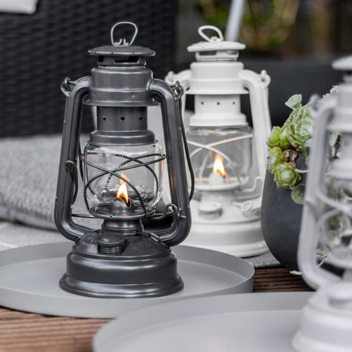 Handcrafted black galvanized oil lantern with thermal heat-resistant globe glowing warmly on gray tray outdoors, perfect for Lamps & Lighting, Camping, and Emergency Supplies collections.