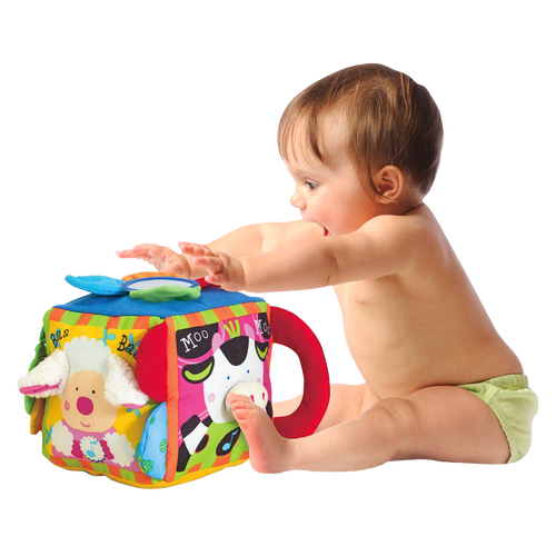 Baby reaching out to play with a soft, colorful musical farmyard cube featuring animal faces, crinkly petals, knotted tags, and a sturdy textured ring for interactive indoor play.