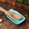 Light blue ceramic spoon rest shaped like a mason jar with a wooden spoon resting on it, set on a wooden countertop near a cutting board and herbs, ideal for kitchen use and easy cleanup.