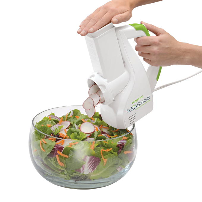 White and green electric vegetable slicer shredding radishes directly into a glass bowl of mixed fresh salad greens and shredded carrots, ideal for Kitchen & Food and Food Prep collections.
