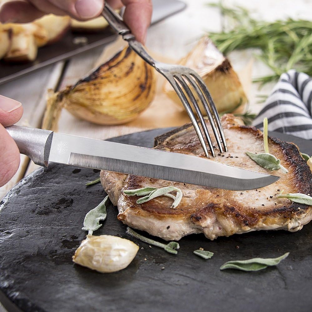 Handcrafted Rada Steak/Utility Knife with high carbon surgical steel blade and solid satin-finished recycled aluminum handle, slicing a grilled pork chop on a rustic surface.