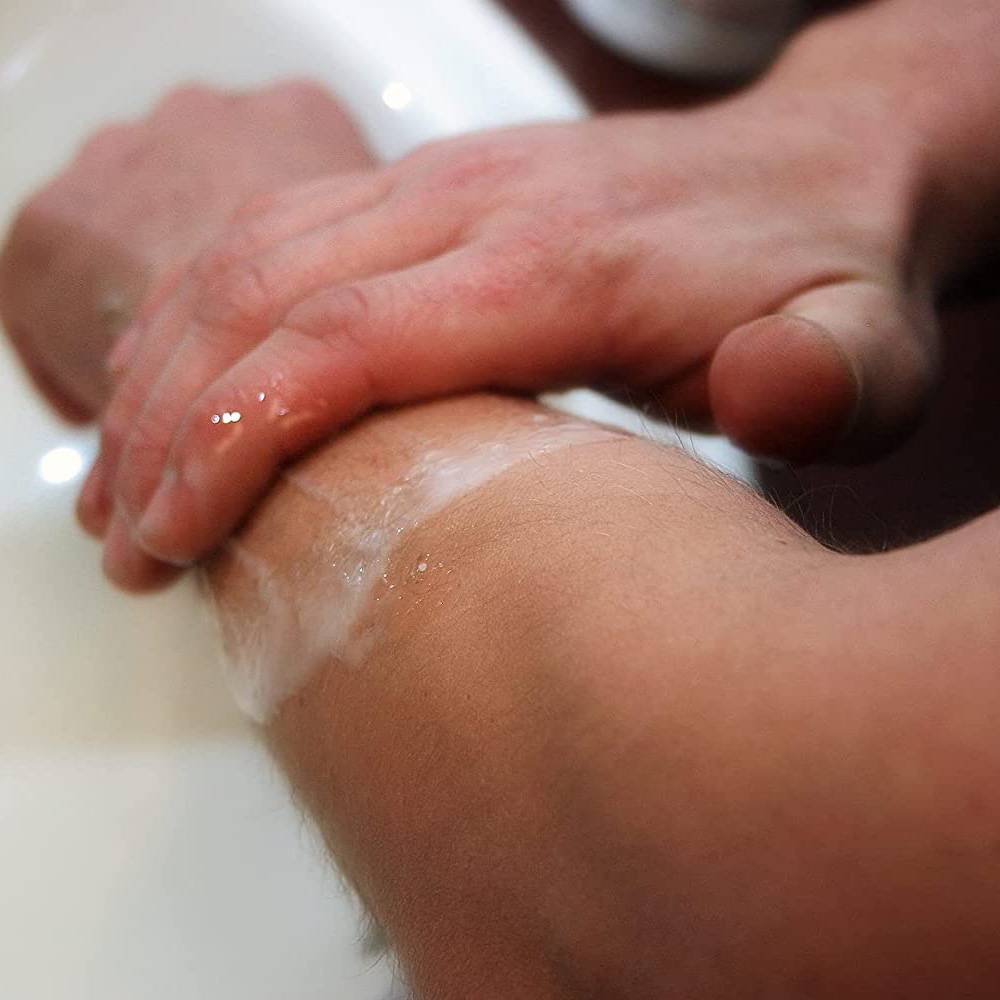 Close-up of hands applying a soothing medicated scrub to an arm under cool water, promoting relief from rash symptoms in Health & Wellness and USA Made collections.