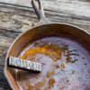 Black rust eraser bar embossed with lettering, resting on a heavily rusted cast iron skillet, illustrating a cleaning utensil from Kitchen & Food and Household Cleaning collections made in USA.