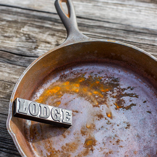 Black rust eraser bar embossed with lettering, resting on a heavily rusted cast iron skillet, illustrating a cleaning utensil from Kitchen & Food and Household Cleaning collections made in USA.
