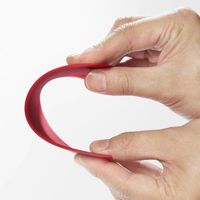 Hand holding a flexible red silicone scraper with a thin metal core, demonstrating its bendable, contoured design ideal for Kitchen & Food, Baking Supplies, and Cooking Helpers collections.