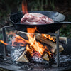 Heavy-duty steel stand supporting a cast iron skillet with raw meat over an open wood fire, ideal for outdoor cooking in Farm, Garden & Tool, Camping, and Best Sellers collections.