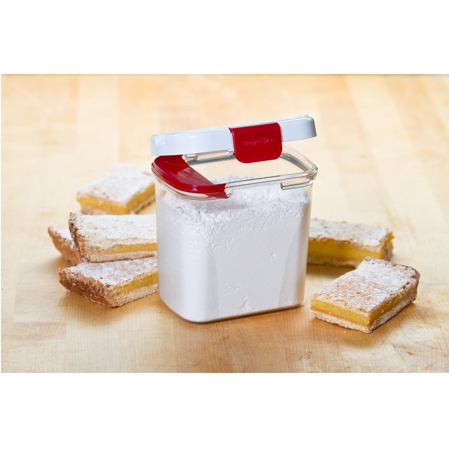 Clear plastic powdered sugar container with red and white lid, featuring a built-in leveler, surrounded by powdered sugar-dusted lemon bars on a wooden surface, showcasing Kitchen & Food and Storage and Serving collections.
