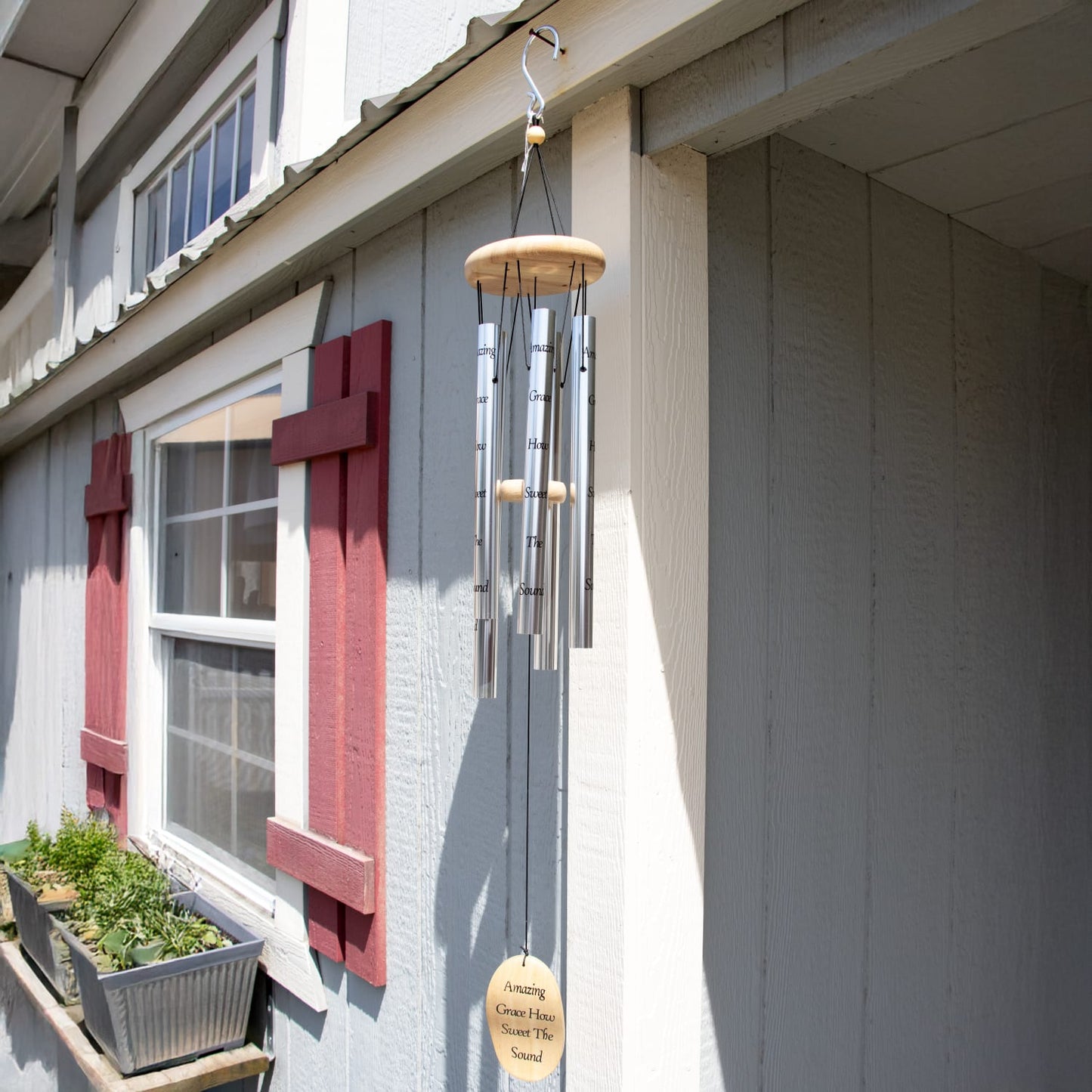 Handcrafted silver windchime with natural wood accents hanging outdoors on a light gray siding wall near red window shutters, ideal for Farm, Garden & Tool, Garden Accessories, and Best Sellers collections.