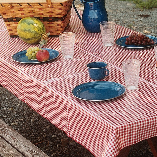 Rectangular vintage vinyl tablecloth with a classic red and white gingham pattern, featuring red merrowed edges, set outdoors with picnic essentials, ideal for Home & Decor and Kitchen Textiles collections.
