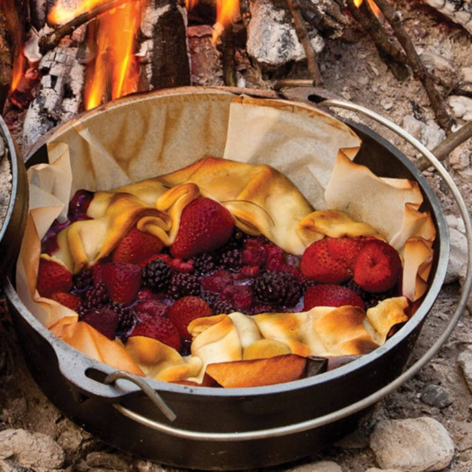 Handcrafted Lodge cast iron camp Dutch oven with built-in legs cooking a mixed berry cobbler outdoors over campfire coals, featured in Farm, Garden & Tool, Camping, Cast Iron, USA Made, Best Sellers, and Promo Eligible collections.