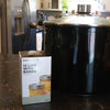 Box of wide-mouth canning jar lids and bands displayed on a kitchen counter next to a large black cooking pot, highlighting essential food preservation supplies.