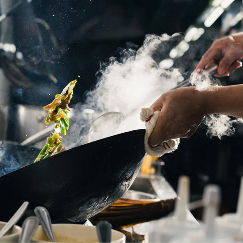 Hands tossing stir-fry vegetables in a steaming wok using long-handled utensils, showcasing kitchen tools ideal for Kitchen & Food and Cooking and Baking Helpers collections.