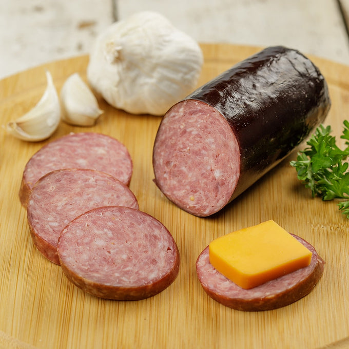 Handcrafted summer sausage from Amish Country, sliced on a wooden board with garlic cloves, fresh parsley, and a slice topped with cheddar cheese, perfect for Kitchen & Food, Pantry, Meats, USA Made, and Best Sellers collections.