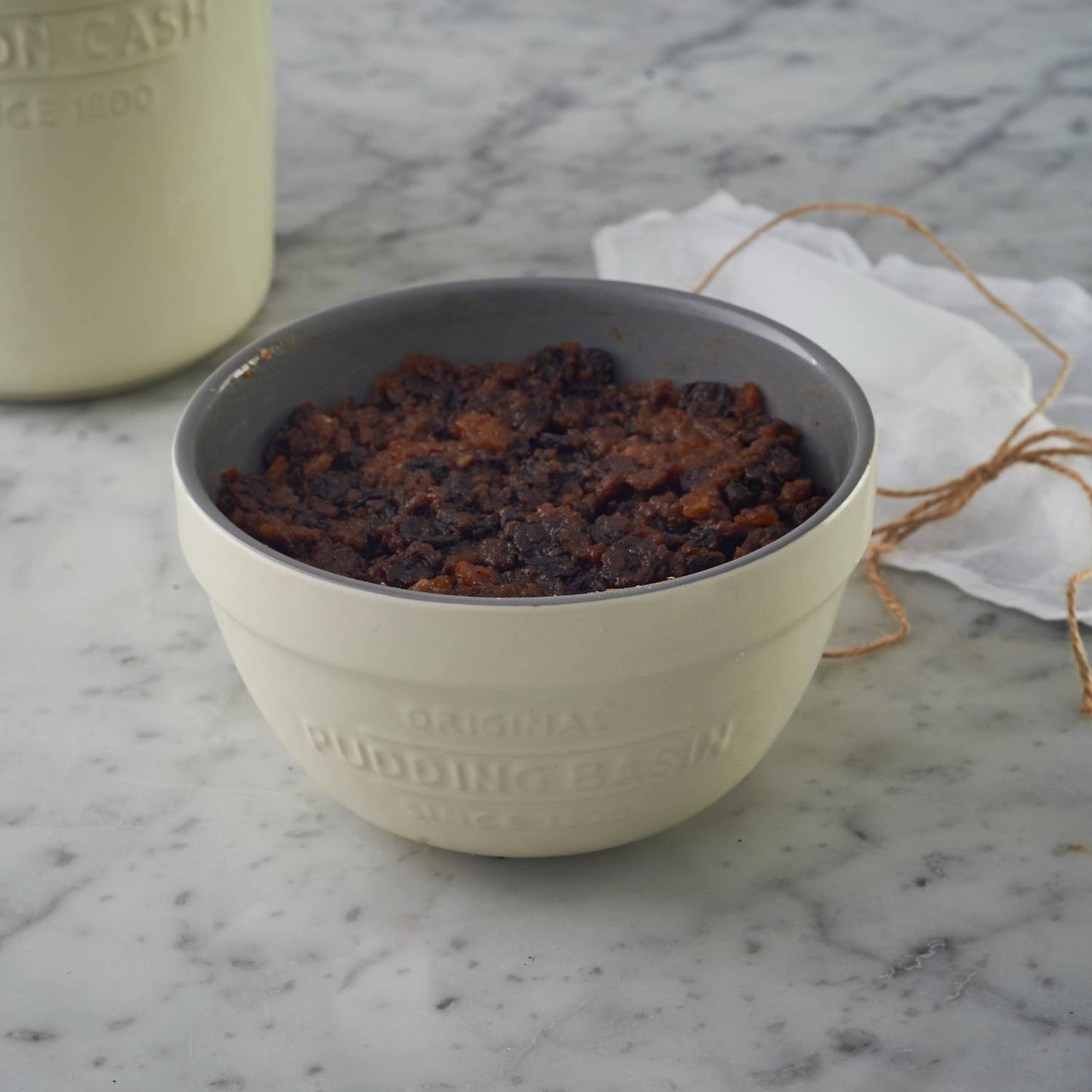 Cream-colored Mason Cash all-purpose bowl filled with a traditional steamed pudding, styled on a marble surface with a rustic twine-tied cloth, ideal for Kitchen & Food, Cookware, Baking Supplies, Storage and Serving, Best Sellers, and Promo Eligible collections.