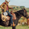 Woman wearing a cowboy hat and casual jacket sitting on a dark brown horse with a saddle bag featuring a cast iron grill pan, set against a grassy outdoor landscape with hills, perfect for Kitchen & Food and USA Made collections.