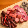 Assortment of smoky cured meats including sliced bologna, chunks of ham, small sausages, and whole chili peppers arranged on parchment, highlighting handcrafted Amish made quality in Kitchen & Food, Food, Meats, USA Made, Best Sellers, and Promo Eligible collections.