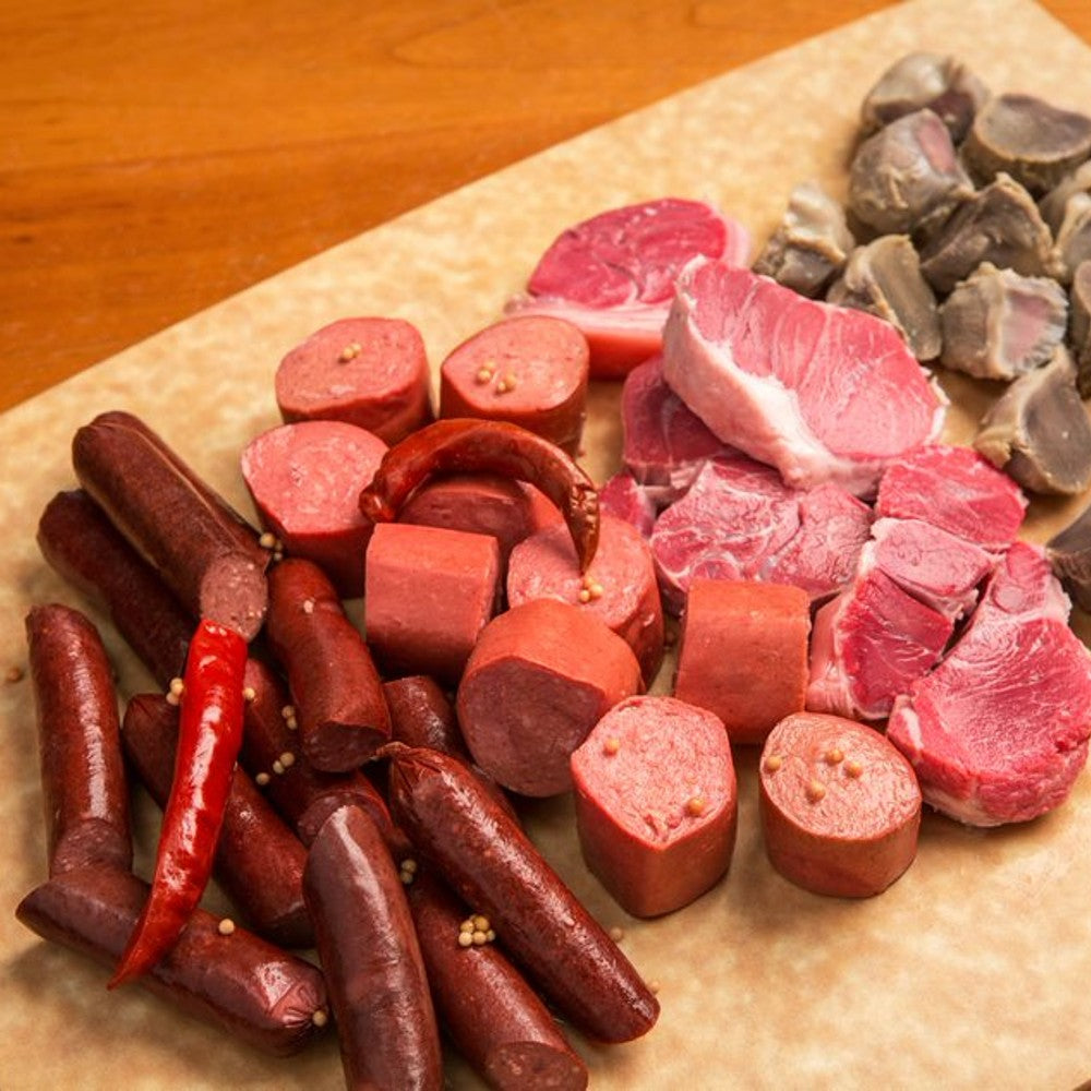 Assortment of smoky cured meats including sliced bologna, chunks of ham, small sausages, and whole chili peppers arranged on parchment, highlighting handcrafted Amish made quality in Kitchen & Food, Food, Meats, USA Made, Best Sellers, and Promo Eligible collections.