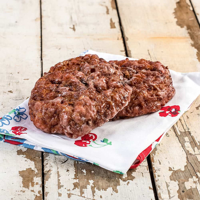 Two freshly baked fruit fritters with a sweet glaze resting on a colorful floral cloth, showcasing a handmade treat perfect for Kitchen & Food, Snacks and Sweets, USA Made, Holiday Hosting, and Best Sellers collections.