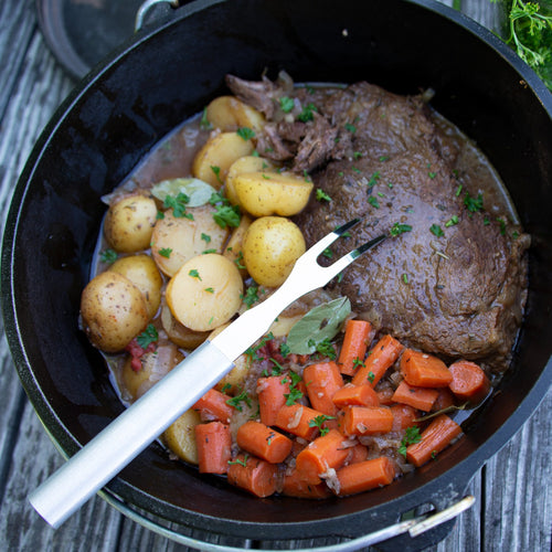 Handcrafted Rada carving fork with long stainless steel tines resting in a cast iron Dutch oven with cooked beef, carrots, and baby potatoes, ideal for Kitchen & Food, Storage and Serving, USA Made, Best Sellers, and Promo Eligible collections.