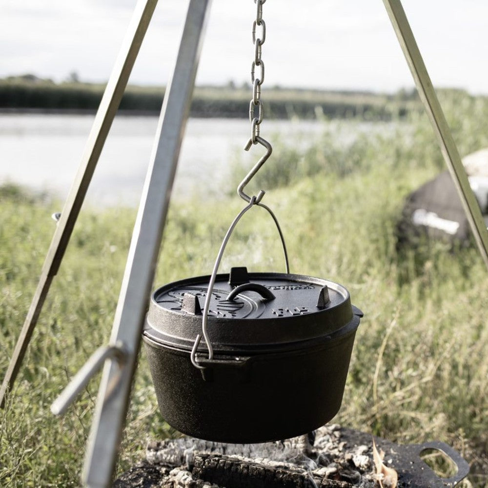 Sturdy cast iron Dutch oven with legs suspended from a tripod over an open fire, featuring a fitted lid with raised details, perfect for Kitchen & Food, Cookware, Cast Iron, Best Sellers, and Promo Eligible collections.