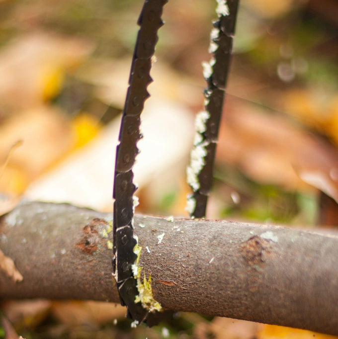 Close-up of a compact pocket-sized chain saw cutting through a small tree branch outdoors, showcasing a sharp, durable tool ideal for camping, wood cutting, and farm use.